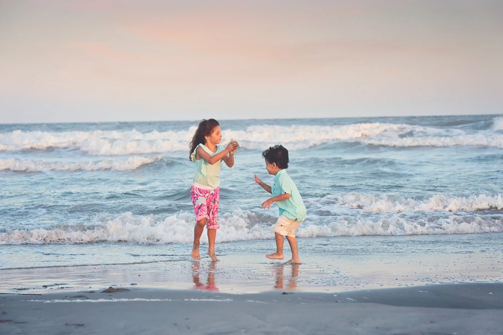 Two children playing together in the ocean waves at sunset